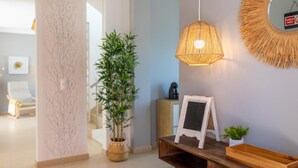 A modern interior with a wooden console table, a hanging woven light fixture, a potted bamboo plant, and a mirror with a sunburst frame. - Villa Soleil by Acasadascasas (Mafra)