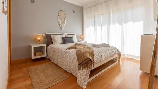 A bedroom with a bed, nightstands, a dreamcatcher, and a large window with curtains. - Villa Soleil by Acasadascasas (Mafra)