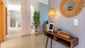 A hallway with a wooden console table, a hanging light fixture, a mirror with a sunburst frame, and a potted plant. - Villa Soleil by Acasadascasas (Mafra)