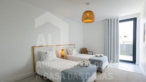 Ein modernes Hotelzimmer mit einem großen Bett, zwei Nachttischen, einer Pendelleuchte und Blick auf die Stadt durch das Fenster.