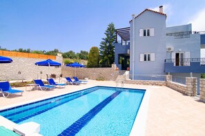 A swimming pool with blue tiles, surrounded by lounge chairs and umbrellas, and a stone wall. - Blue Villa 2 - With Private Pool (Mylopotamos)
