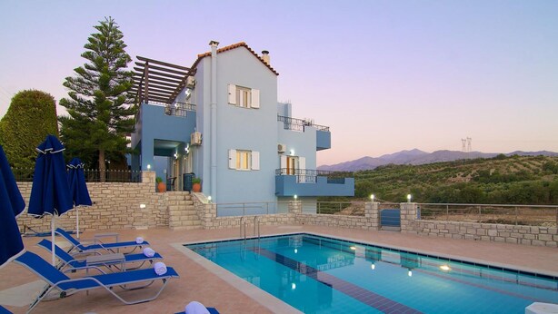 A modern building with a pool area, including lounge chairs and umbrellas, overlooking a hilly landscape. - Blue Villa 2 - With Private Pool (Mylopotamos)