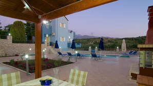 A pool area with lounge chairs, a table with a chessboard, and a view of a building with a balcony. - Blue Villa 2 - With Private Pool (Mylopotamos)