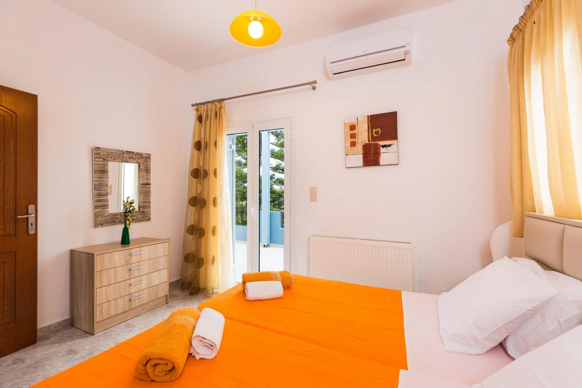 Una camera da letto con un letto, una cassettiera, uno specchio, un condizionatore d'aria e una finestra con tende.