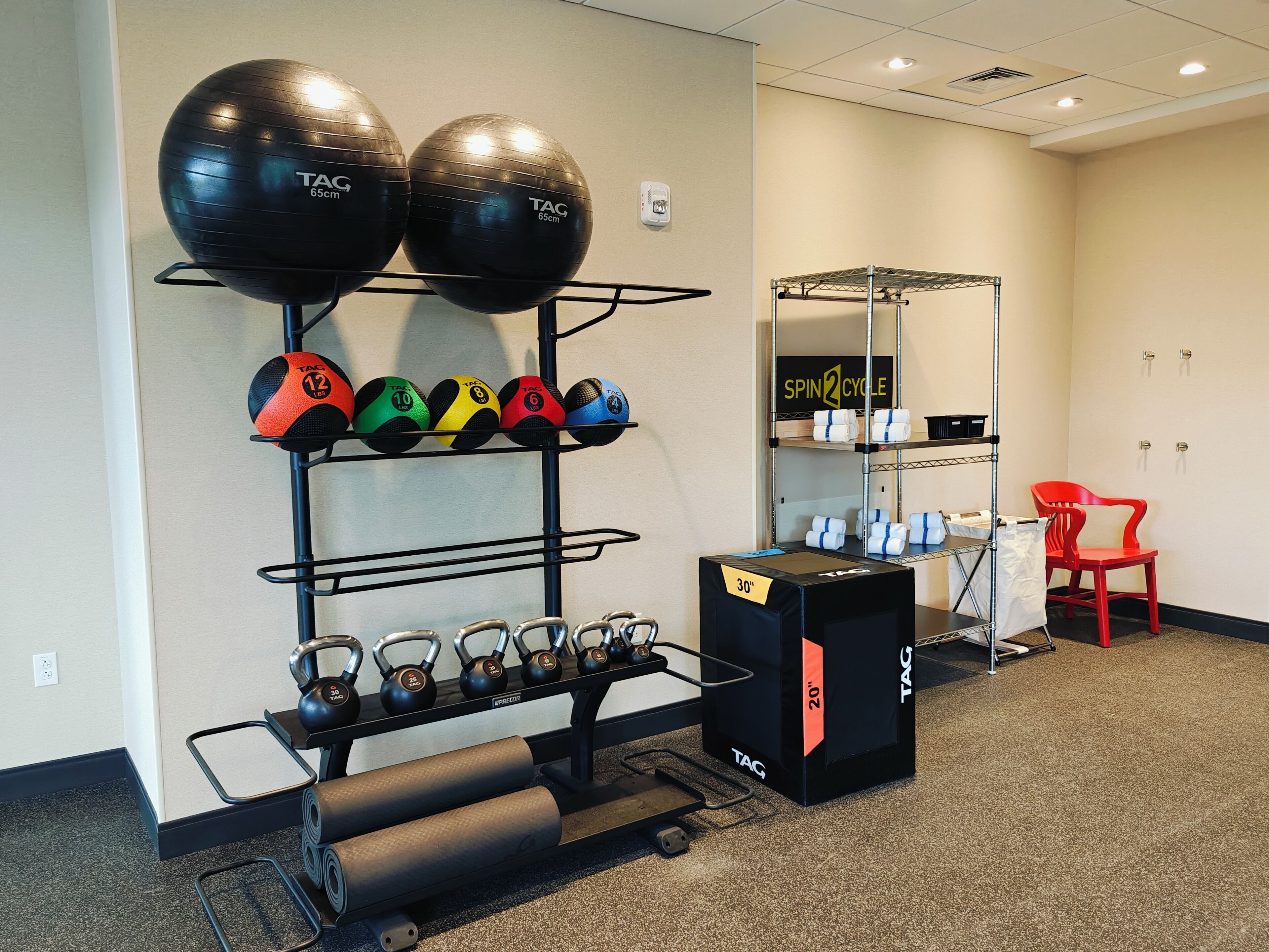 Een sportschoolruimte met trainingsapparatuur, waaronder kettlebells, medicine balls en een spinningfiets.