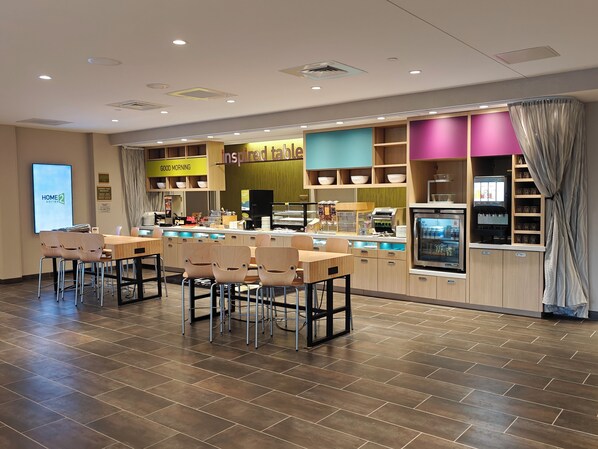 A modern breakfast area with a counter, seating, and a refrigerator. - Home2 Suites by Hilton Bristol (Bristol)