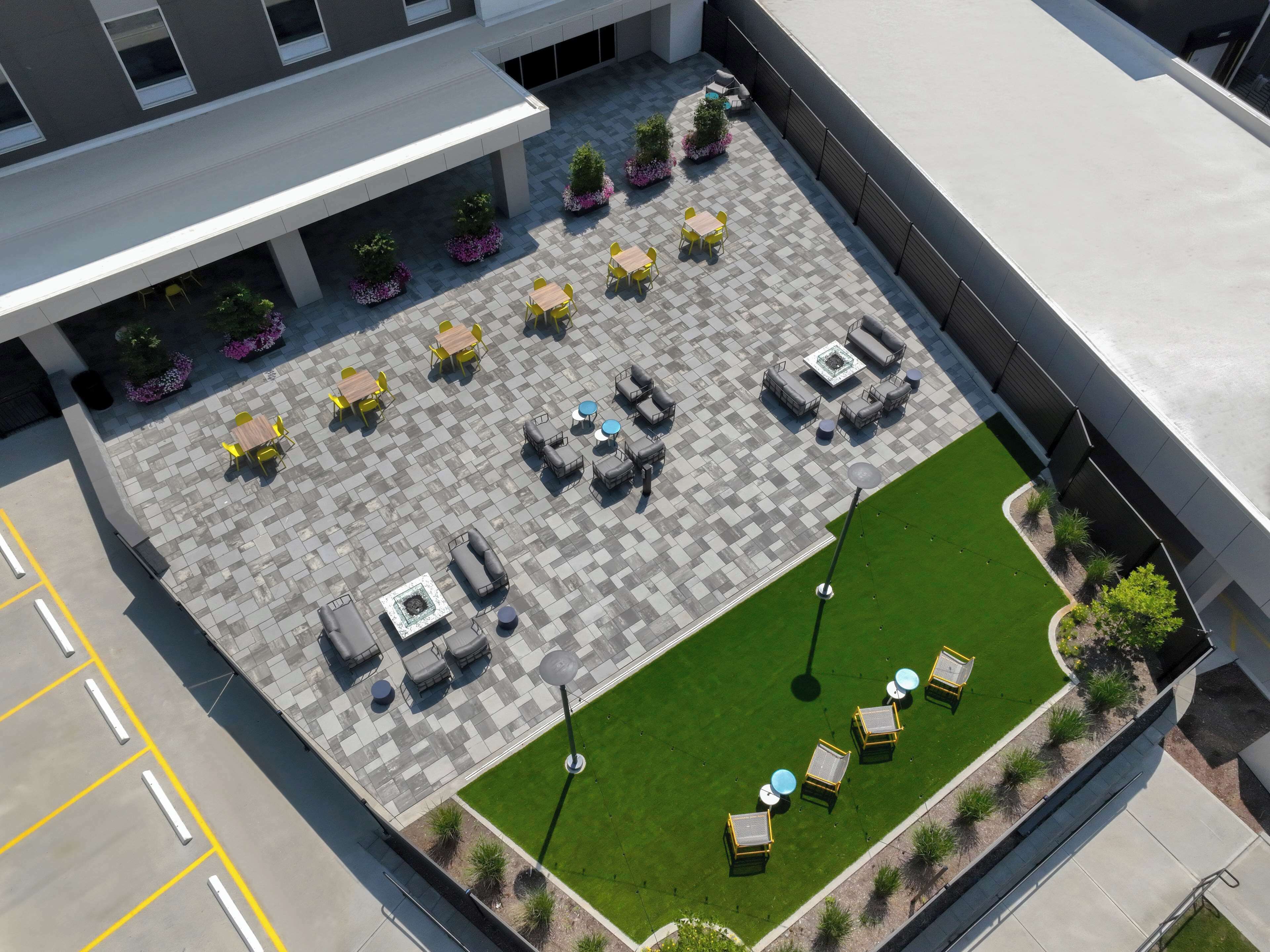 Un patio al aire libre con varias opciones de asientos, incluyendo mesas y sillas, y un pequeño césped.