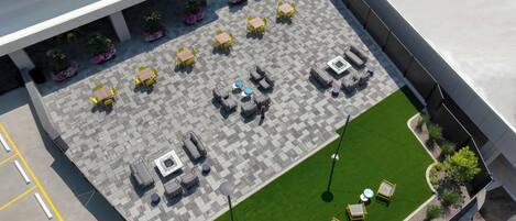 Un patio al aire libre con varias opciones de asientos, incluyendo mesas y sillas, y un pequeño césped.