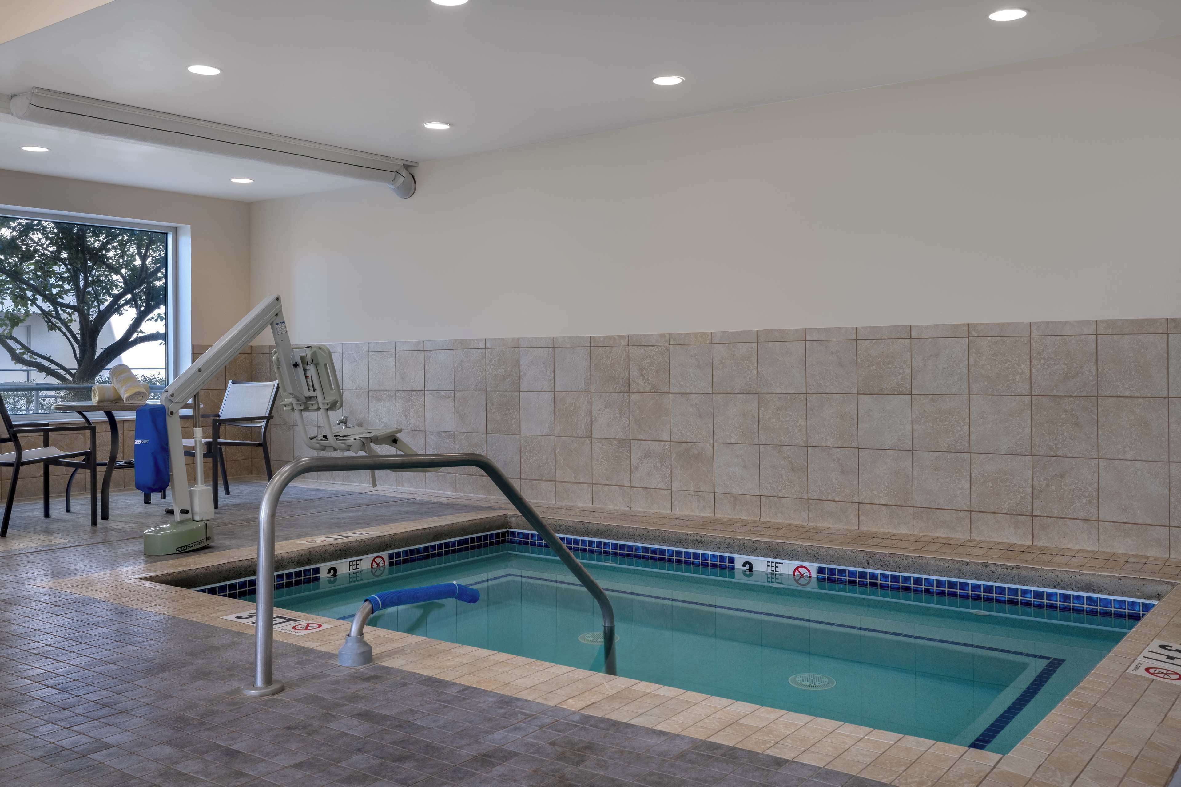 An indoor swimming pool with a tiled wall, a pool ladder, and a blue pool edge.