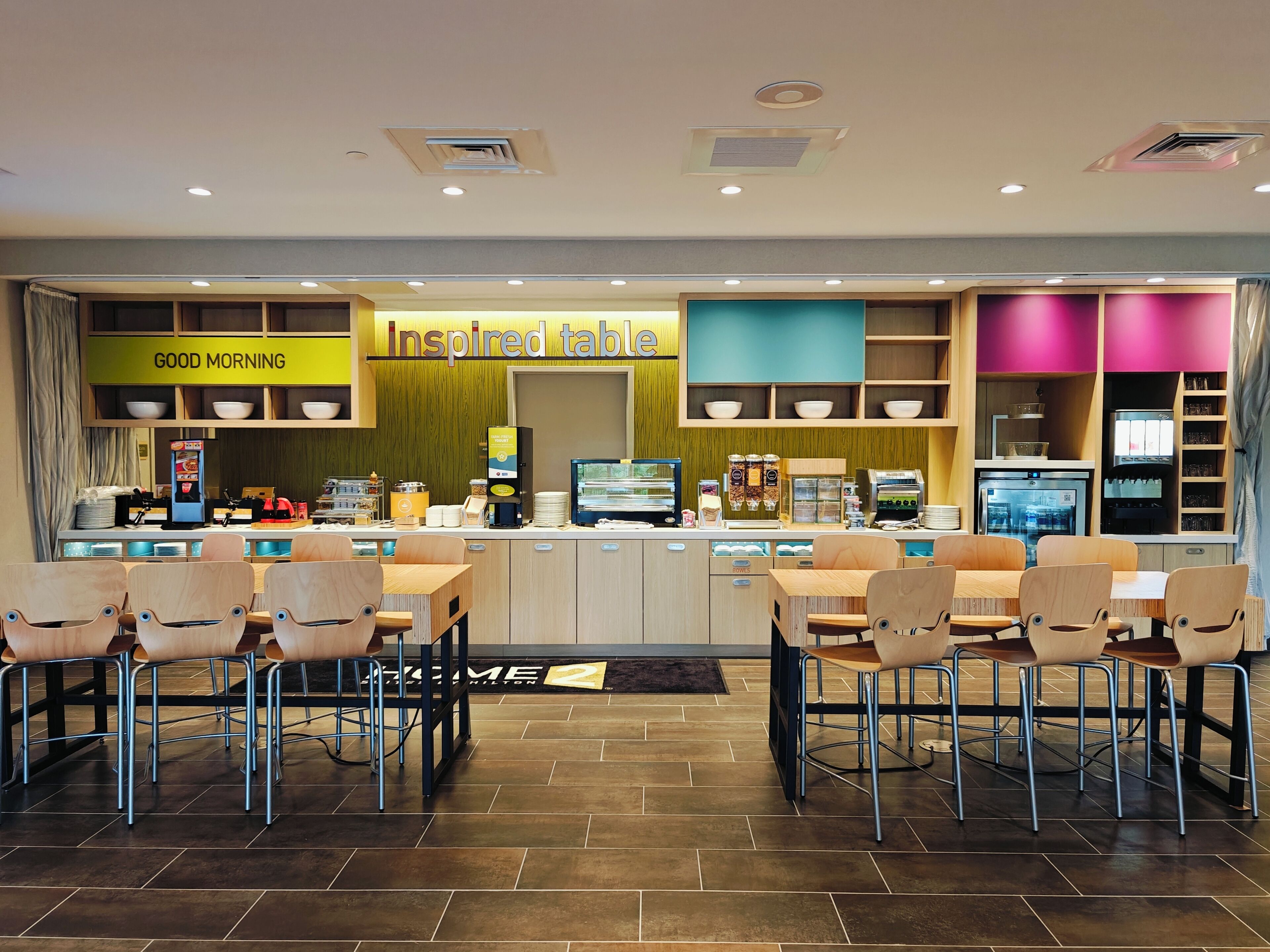 A modern cafe with a central counter, seating area, and various food and drink stations.