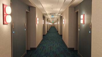 Un pasillo de hotel con pisos alfombrados, paredes de color claro y apliques de luz.