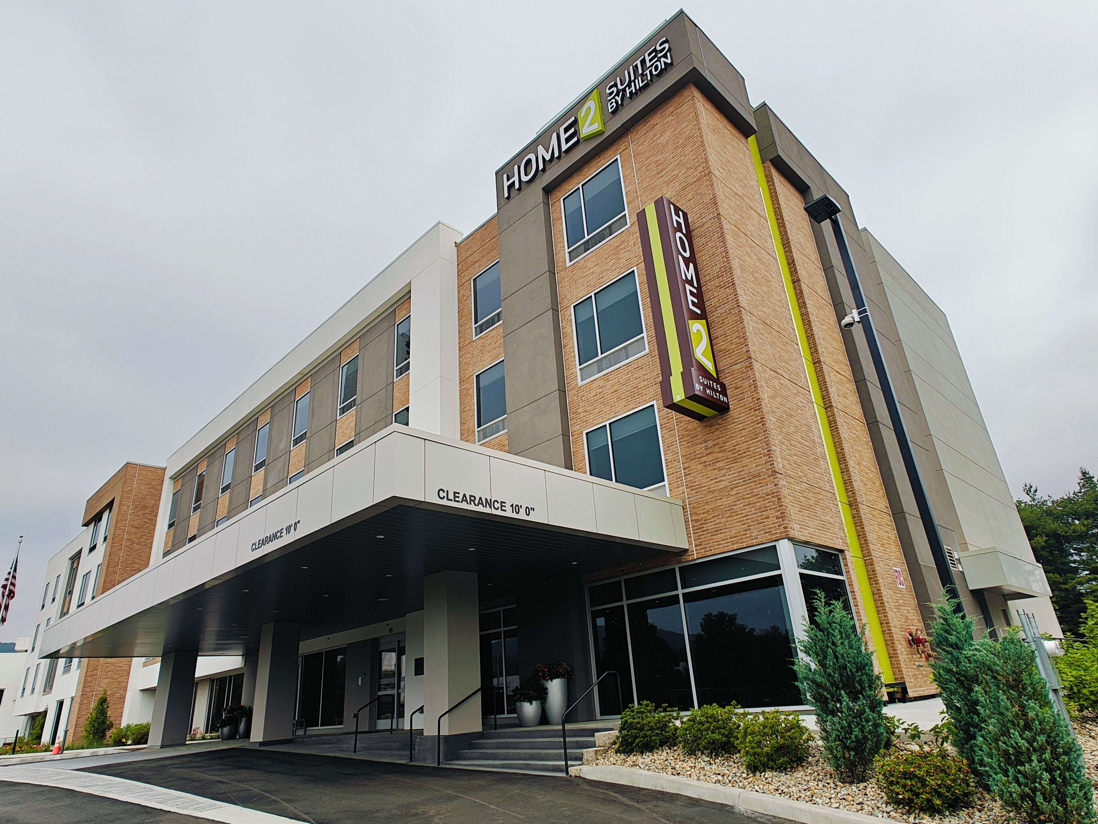 Un hôtel au design moderne, avec une entrée bien visible, une enseigne indiquant « Home 2 Suites by Hilton » et un panneau indiquant une « hauteur libre de 10 pieds » (environ 3 mètres).