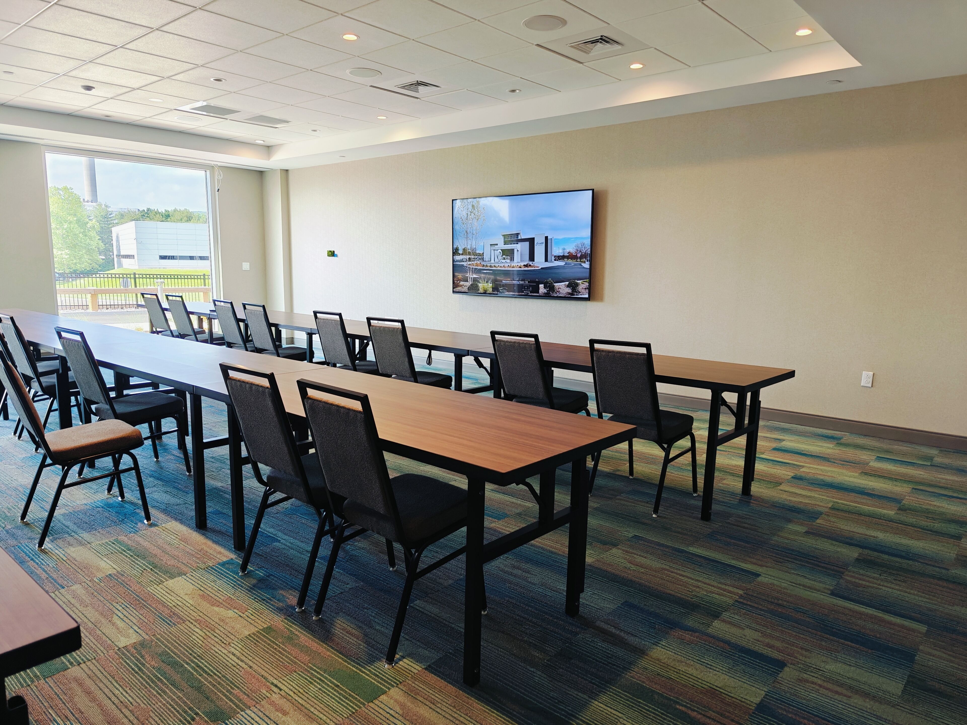 A conference room with a long table, chairs, and a large window with a view of buildings and trees.