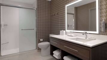 Une salle de bain moderne dotée d’une douche à parois de verre, de toilettes blanches, d’un grand miroir et d’un meuble-lavabo avec un espace pour ranger les serviettes.