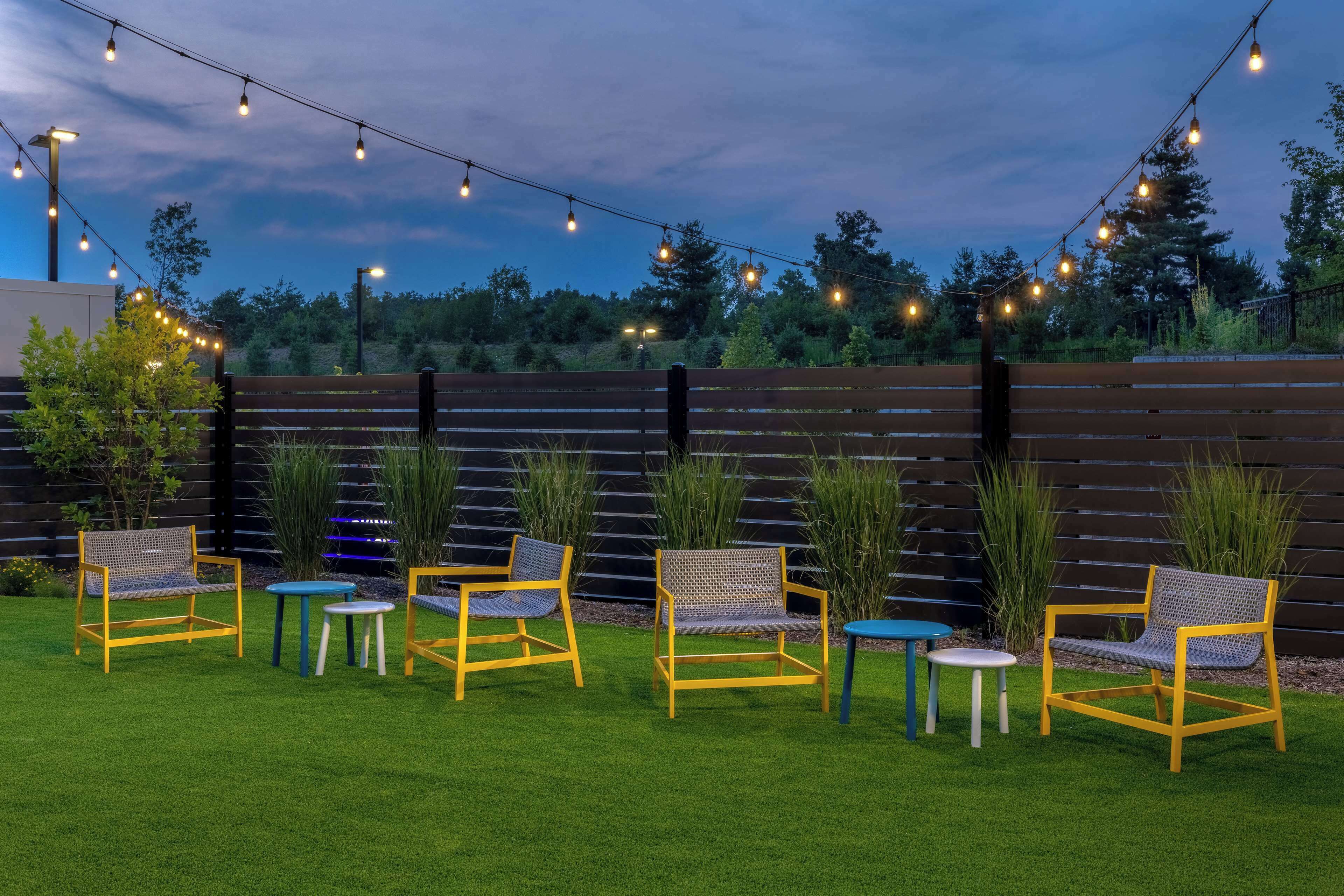 Un espace extérieur aménagé avec des chaises et des tables, des guirlandes lumineuses et une clôture en bois.