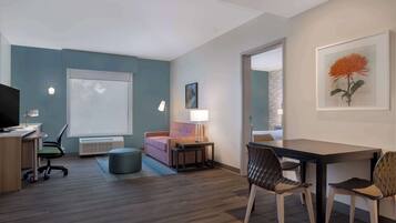 A modern hotel room with a desk, chair, sofa, and a dining table with chairs.