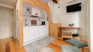 A compact kitchen with white cabinets, a microwave, and a stove. There's a wooden bench and a small table with a plant. - Bonjardim City Flats - Relaxing Terrace (Porto)
