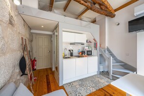 Une cuisine compacte avec des meubles blancs, un four à micro-ondes et un évier. Un escalier en bois mène à un niveau supérieur.
