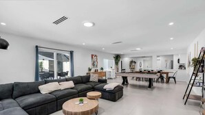 Ein modernes Wohnzimmer mit einem Ecksofa, einem Couchtisch und einem Essbereich, im Hintergrund eine Küche.