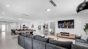 Ein modernes Wohnzimmer mit einem grauen Ecksofa, einem Essbereich mit Holztisch und Stühlen, einem an der Wand montierten Fernseher und einem Stadtbild.