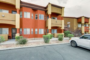 A multi-story residential building with balconies, a parking area, and a white car parked in front.