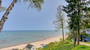 A beach view with a small cabin, a picnic table, and a blue tarp on the sand. - Beachy Palms Cottage on Lake Huron w/ Hot Tub! (Palms)