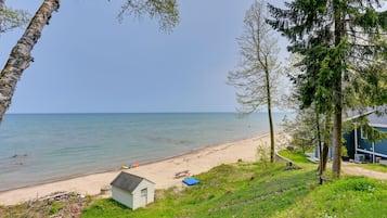 A beach view with a small cabin, a picnic table, and a blue tarp on the sand.