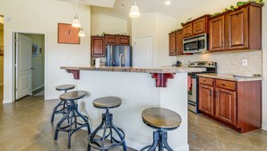 A kitchen with wooden cabinets, a stainless steel refrigerator, a microwave, and a built-in oven. There are three stools under the island. - Mesquite Vacation Rental - Close to Golf Courses! (Mesquite)