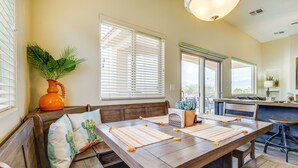 A dining area with a wooden table set for four, benches on either side, and a large window with blinds. - Mesquite Vacation Rental - Close to Golf Courses! (Mesquite)