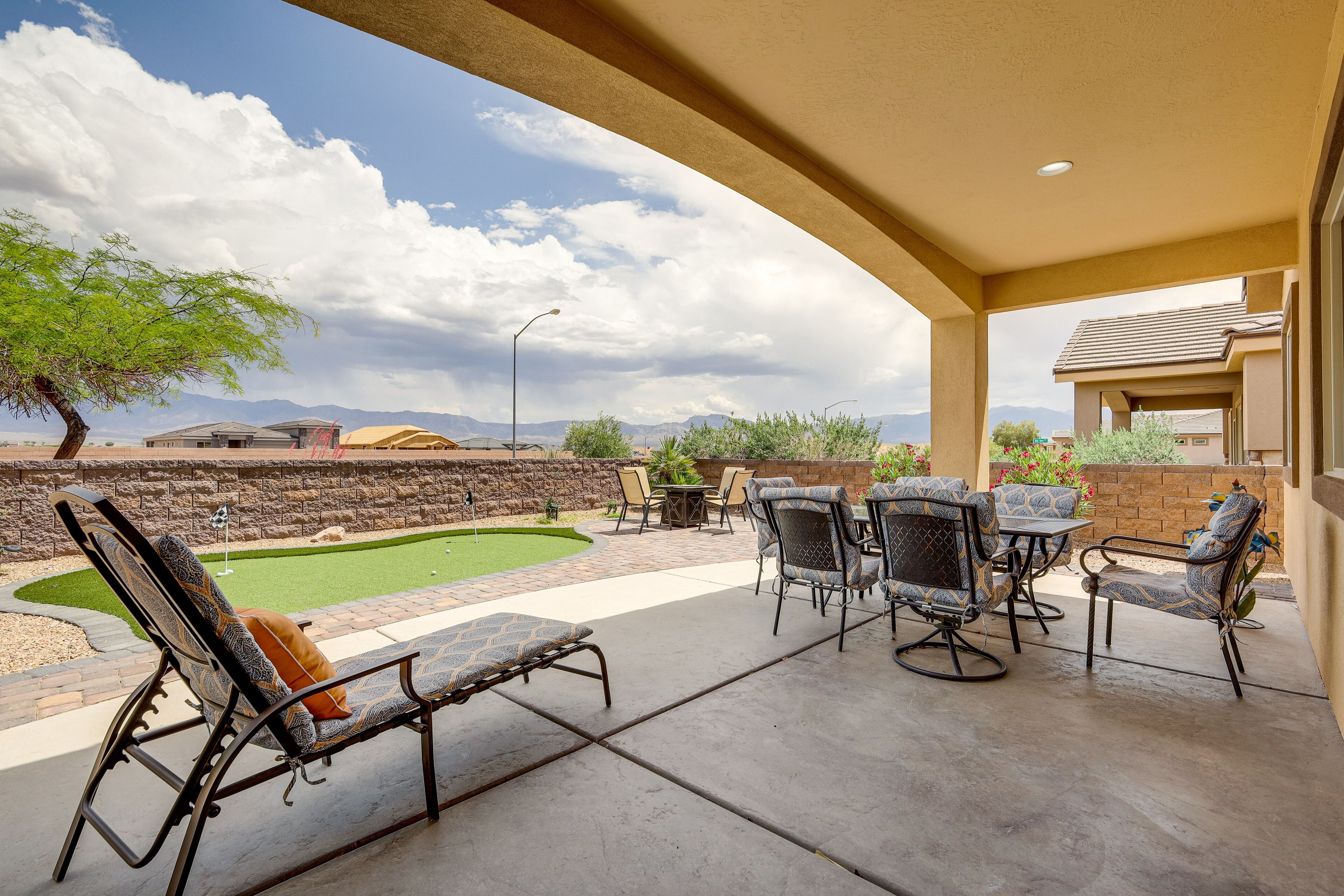 A covered patio with outdoor furniture, a small lawn, and a stone wall.