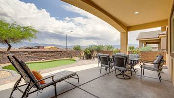 A covered patio with outdoor furniture, a small lawn, and a stone wall.
