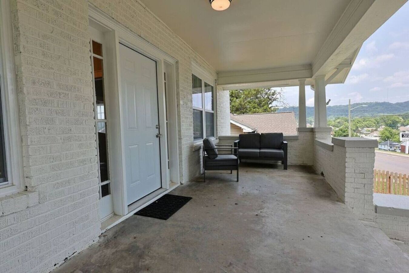A covered porch with a concrete floor, a white door, and two black chairs.