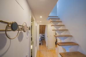 A modern staircase with wooden steps and a glass enclosure. A hallway with a wooden floor and a white wall with a circular mirror. - Nomad s Downtown Lisbon - 3bdr Augusta Classica (Lisbon)