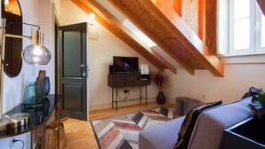 Une chambre à coucher confortable, aménagée en mezzanine, avec des poutres apparentes, une grande fenêtre, un téléviseur et un décor moderne.