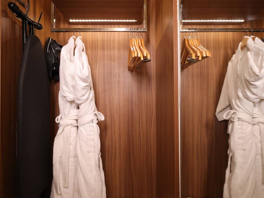 Un baño de hotel con paneles de madera, un perchero, una bata y zapatillas sobre el mostrador.
