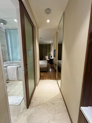 A hotel corridor with a bathroom on the left, a bedroom with a bed and a desk, and a mirror reflecting the room. - Fairfield by Marriott Agra (Agra)