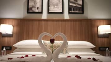 A hotel room with a bed, a heart-shaped towel arrangement, and a rose. There are three framed pictures on the wall above the bed.