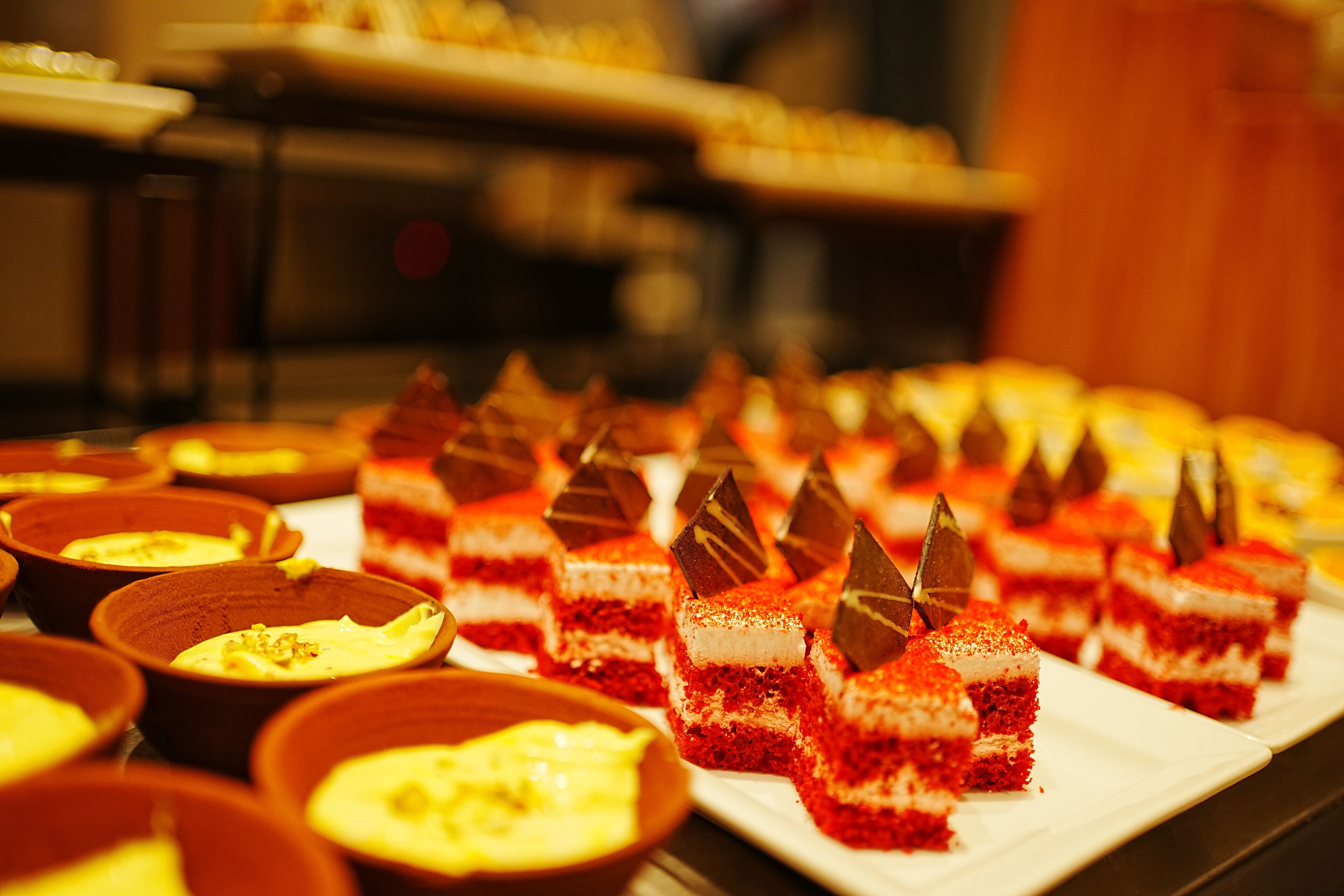 Una presentación de postres, incluyendo rebanadas de pastel de terciopelo rojo con decoraciones de chocolate, dispuestas sobre un plato blanco.