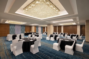 Meetings and events take place in this stylish conference room, featuring a large chandelier, round tables, and comfortable seating.