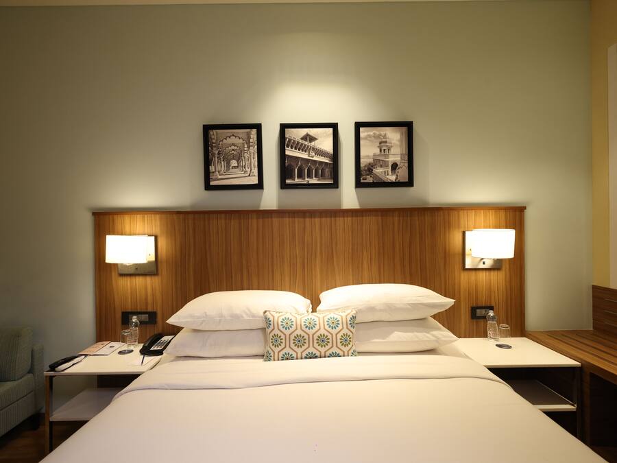 A hotel room with a large bed, two bedside tables, a nightstand, a lamp, a telephone, a water bottle, and three framed pictures on the wall.