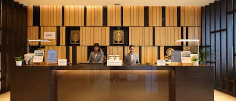 A reception desk with two staff members, wooden paneling, and framed artwork.