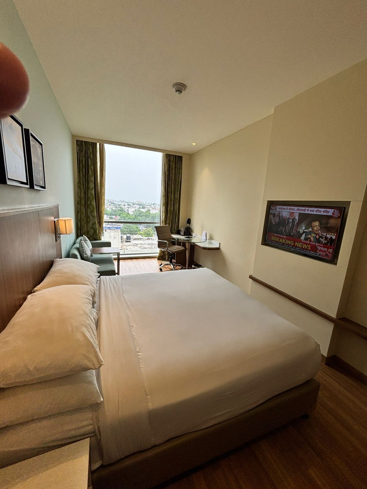 A hotel room with a large bed, a desk, a chair, a window with a view of the city, and a framed picture on the wall.