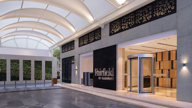 Interior de hotel con diseño moderno, que incluye una entrada de vidrio, una recepción y un área de descanso con un muro decorado.