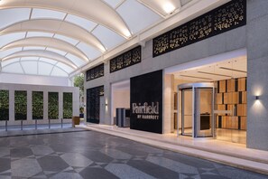 Ein Hotelinterior im modernen Stil, mit Glastür, Rezeption und einer Sitzecke mit Wandverkleidung.