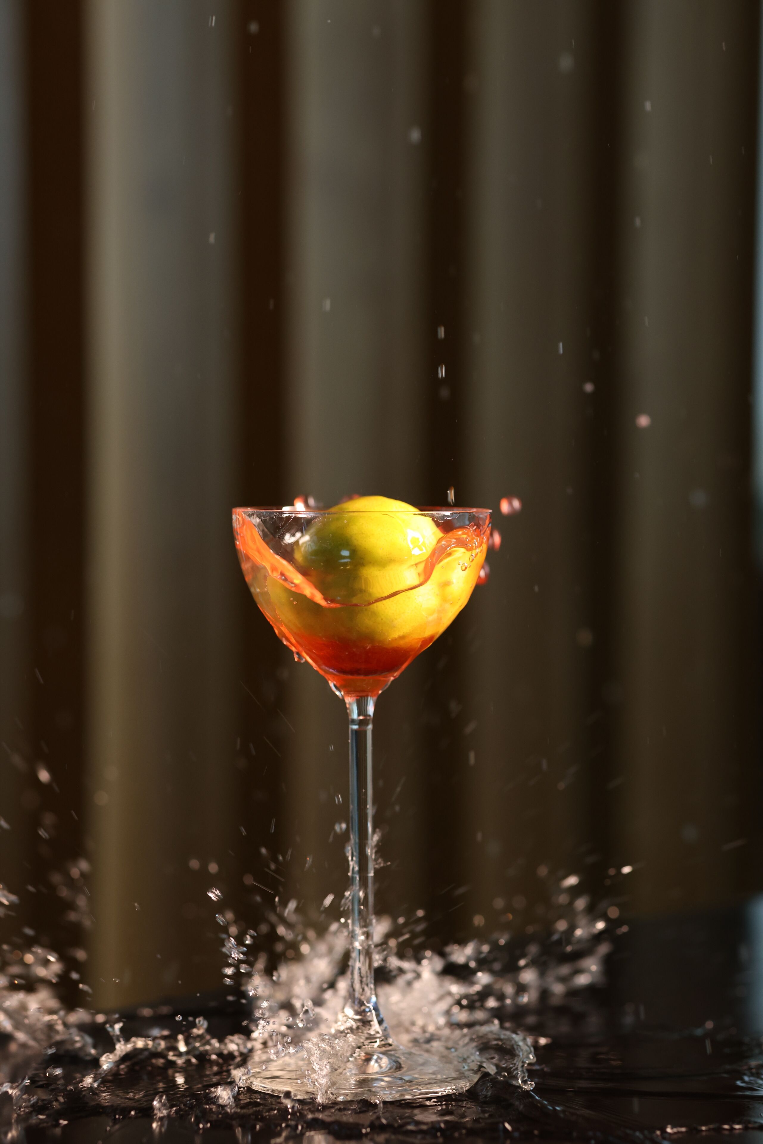 Un verre à martini orné d’une tranche de citron sur le bord, avec de l’eau qui éclabousse, le tout sur un fond sombre.