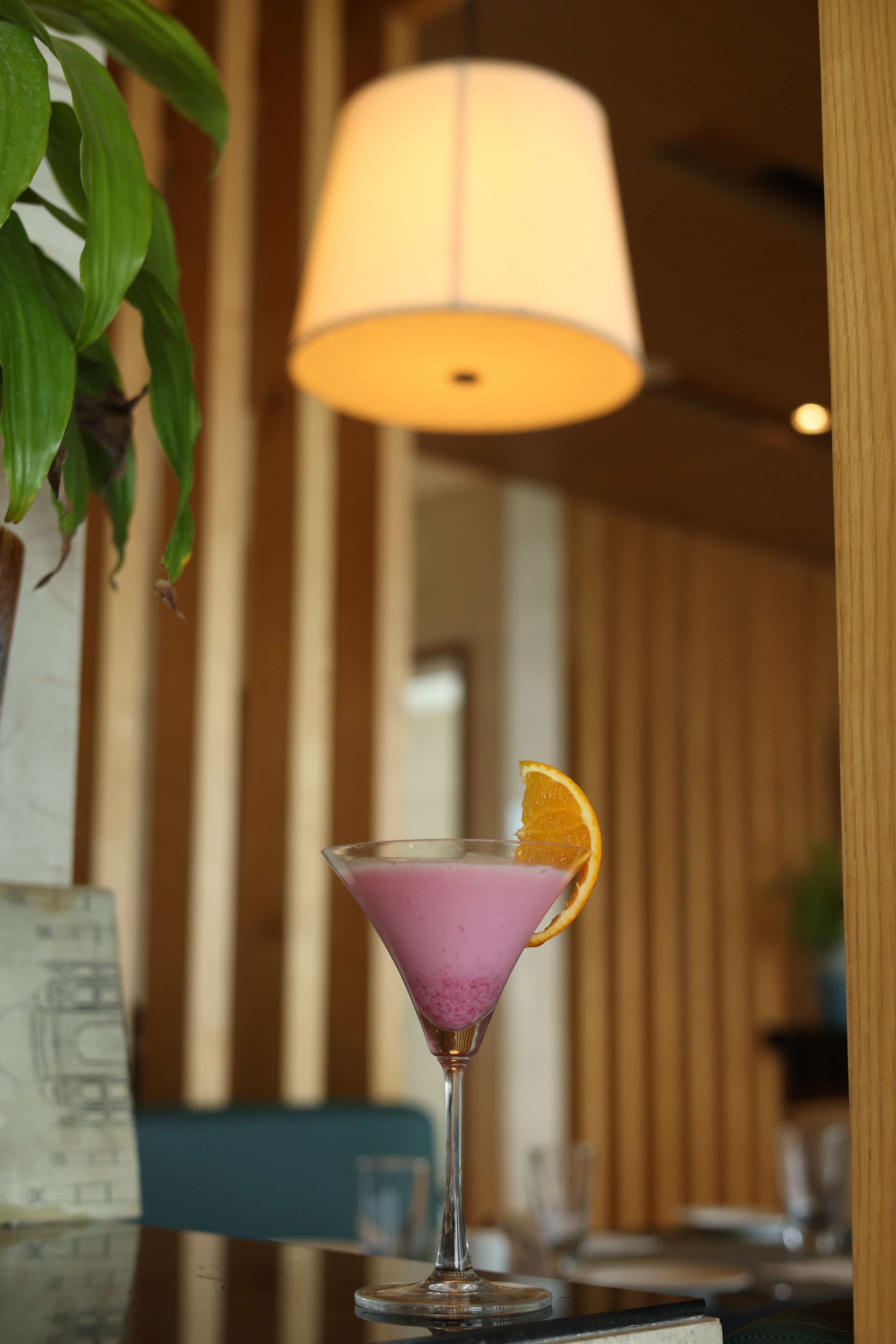 A martini glass with a purple drink and an orange garnish on a table.