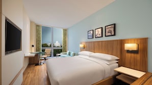 Habitación de hotel con una cama grande, televisión, escritorio y vistas a un edificio a través de la ventana.