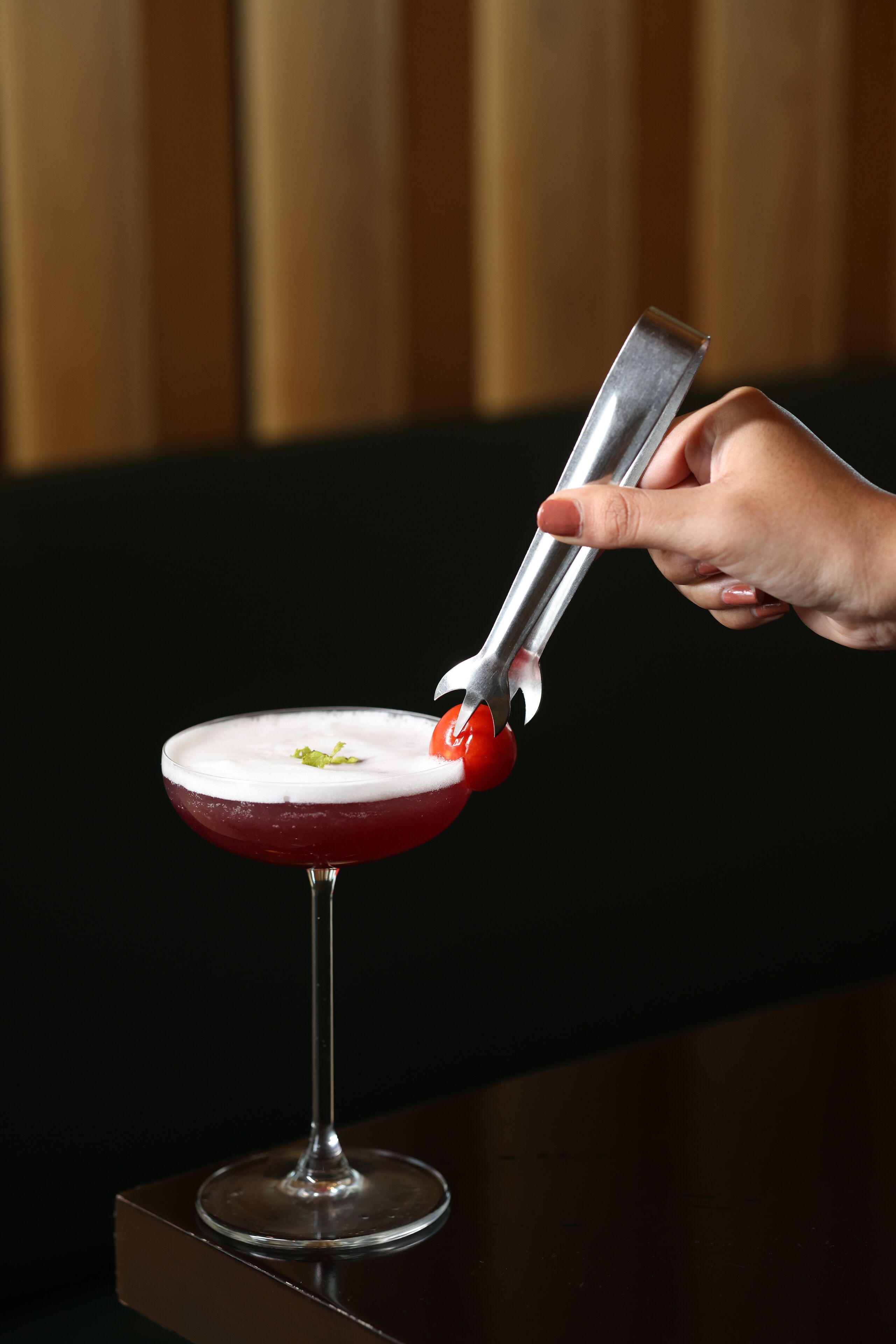 En hand använder ett metallverktyg för att dekorera en cocktail i ett martiniglas.