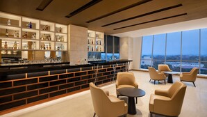 Un bar moderno con techo alto, amplios ventanales y vista a la ciudad.