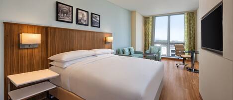 A hotel room with a large bed, bedside tables, a desk, and a chair. There are three framed pictures on the wall and a TV on the wall.